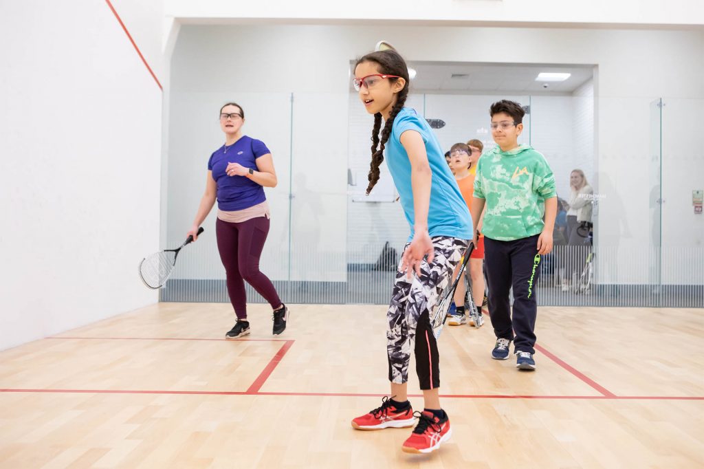 An adult female coaching coaches junior squash players on court